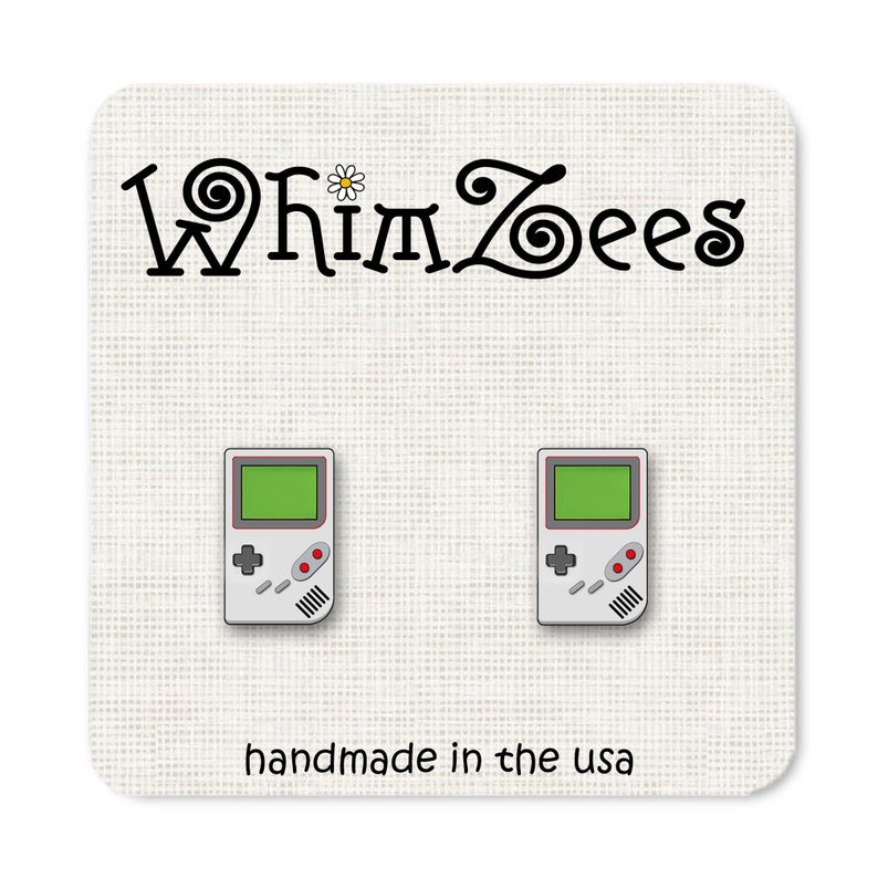 May include: A pair of silver-colored earrings shaped like a vintage handheld video game console. The earrings are on a white background with the text "Whimzees" and "handmade in the USA".
