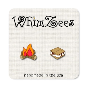 Puede incluir: Un par de pendientes caprichosos con una fogata y un s'more. Los pendientes están hechos a mano en los Estados Unidos.