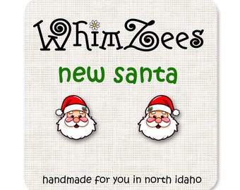 May include: A pair of earrings featuring a cartoon Santa Claus with a red hat, white beard, and a green holly sprig. The earrings are handmade and say "Whimzees new santa" on the card.