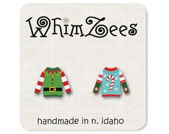 May include: A pair of handmade Christmas-themed earrings featuring a green elf sweater and a blue sweater with a candy cane. The earrings are made by WhimsZeEs and are handmade in Idaho.