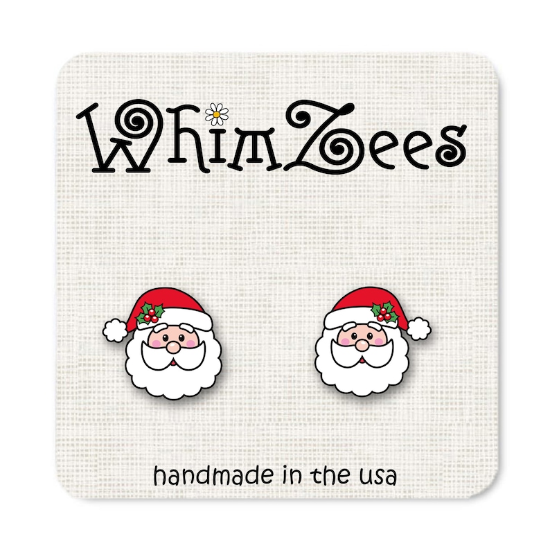 May include: A pair of Santa Claus earrings with red hats, white beards, and black eyes. The earrings are handmade in the USA and feature the text "Whimzees".