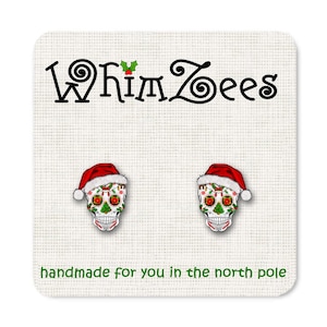 May include: A pair of silver stud earrings featuring a sugar skull design with a Santa hat. The skull is decorated with colorful flowers and green leaves. The earrings are handmade and say "Whimzees" on the card.