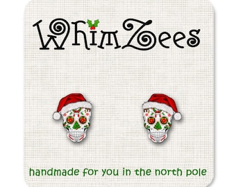 May include: A pair of silver stud earrings featuring a sugar skull design with a Santa hat. The skull is decorated with colorful flowers and green leaves. The earrings are handmade and say "Whimzees" on the card.