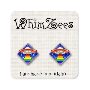 May include: A pair of rainbow pride UFO earrings. The earrings are made of metal and have a blue background with stars and a rainbow stripe. The text "WhimZeEs" and "handmade in n. idaho" are visible on the card.