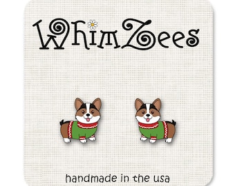 May include: A pair of earrings featuring a cartoon corgi wearing a green and red sweater. The earrings are handmade in the USA and are sold by the company Whimsy Tees.