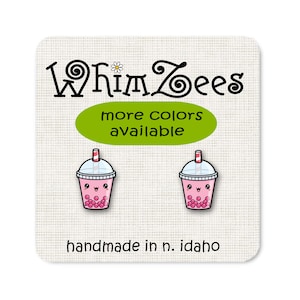 Może przedstawiać: Para różowych kolczyków w kształcie bubble tea z uroczą kreskówkową buźką i słomką. Kolczyki są ręcznie robione w Idaho i dostępne są w innych kolorach. "WhimZeEs" jest napisane na górze obrazka.