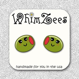 May include: A pair of olive-shaped earrings with smiling faces and red accents. The earrings are on a white card with the text "WhimZees" and "handmade for you in the usa". The background has a dotted pattern.