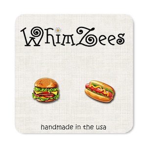 May include: A pair of earrings featuring a cartoon hamburger and hot dog. The earrings are handmade in the USA and are sold by the shop WhimsZeEs.