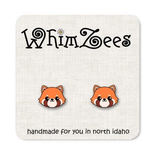 May include: A pair of red panda earrings with black eyes and a white nose. The earrings are handmade and feature the text "WhimZeEs" and "handmade for you in north idaho".