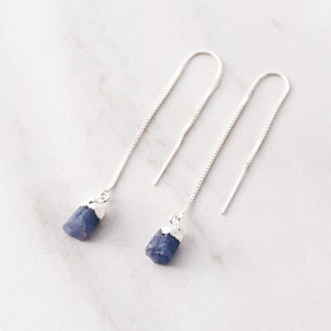 May include: A pair of silver chain earrings with blue gemstone drops. The gemstones are irregular in shape and have a rough, natural texture.