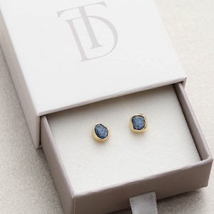 May include: A pair of gold stud earrings with blue gemstone accents in a white box with the letter "TD" printed on the top.