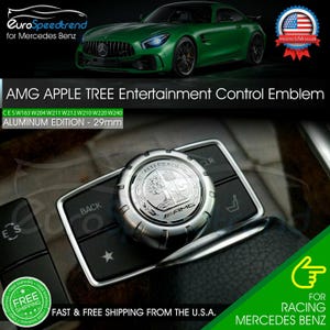 May include: Silver AMG Apple Tree Entertainment Control Emblem, 29mm, for Mercedes Benz. The emblem is made of aluminum and features the AMG logo and the text "ASFALTEREACH". The image also shows a green Mercedes Benz car.