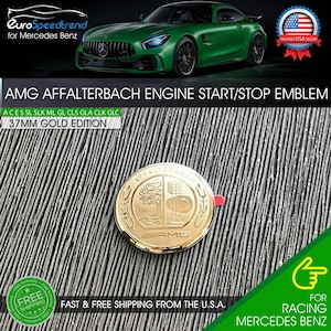 May include: Gold-colored AMG Affalterbach engine start/stop emblem. The emblem is round, with the text "AMG" and "AFFALTERBACH" visible. The emblem is 37mm in diameter and is a gold edition.