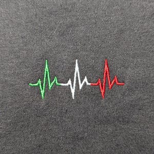 Könnte beinhalten: Ein schwarzes T-Shirt mit einem gestickten Herzschlagmuster in Grün, Weiß und Rot.