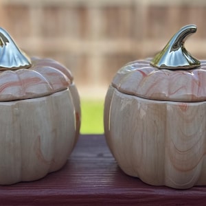 May include: Four ceramic pumpkin-shaped containers with lids. The containers are in different sizes and colors: light blue, beige, beige with gold accents, and orange.