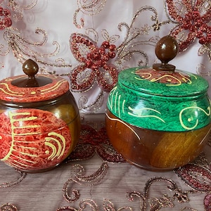 May include: Two wooden lidded boxes with hand-painted designs. One box is painted with red and yellow swirls, the other is painted with green and yellow swirls.
