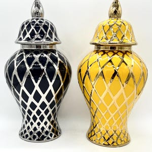 Pode incluir: Dois vasos decorativos de cerâmica com tampas. Um vaso é preto com um padrão de losangos prateados, e o outro é amarelo com um padrão de losangos dourados. Ambos os vasos têm uma forma bulbosa e um remate prateado ou dourado na tampa.