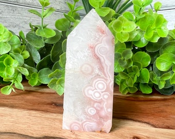 May include: A white and pink agate tower with a pointed top and a natural, rough texture. The tower has a swirling pattern of white and pink agate.