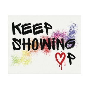 Könnte beinhalten: Weißer rechteckiger Druck mit den Worten „KEEP SHOWING UP“ in schwarzer Schrift im Graffiti-Stil. Bunte Farbspritzer in Regenbogenfarben und ein rotes Herz mit den Buchstaben „UP“ vervollständigen das Design.