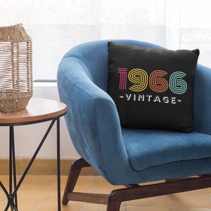 May include: A black throw pillow with a colourful 1966 vintage design. The pillow is sitting on a blue armchair.