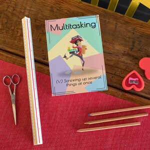 May include: A colorful book with the title "Multitasking" and the text "(V) Screwing up several things at once". The cover features a cartoon illustration of a woman juggling multiple tasks, including a cup of coffee, a book, a phone, and a briefcase.