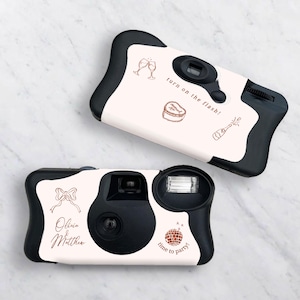 Puede incluir: Dos cámaras desechables con cuerpo blanco y ribete negro. La cámara superior tiene un brindis con copas de champán, un pastel con la palabra "comprometido" en él y una botella de champán que explota. El texto "¡enciende el flash!" está escrito en la cámara. La cámara inferior tiene un lazo, el texto "Olivia & Matthew", una bola de discoteca y el texto "¡hora de la fiesta!"