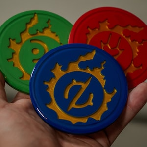 May include: Three round, colorful coasters with a gold flame design and a different symbol in the center of each. The coasters are green, blue, and red.