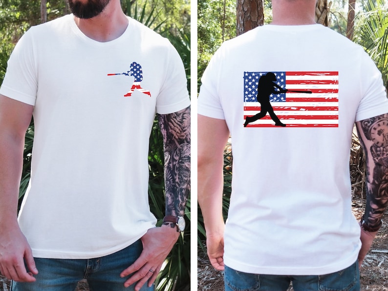 May include: White t-shirt with a baseball player silhouette holding a bat in front of an American flag on the front. The back of the shirt features a distressed American flag with a baseball player silhouette holding a bat.