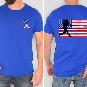 May include: A royal blue t-shirt with a baseball player silhouette in front of an American flag on the front and a baseball player silhouette in front of a distressed American flag on the back.