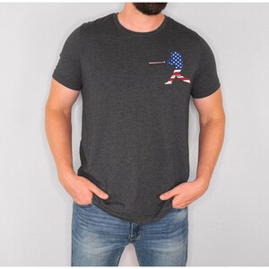 May include: A dark grey t-shirt with a baseball player silhouette printed on the left chest. The player is silhouetted in the colours of the American flag.