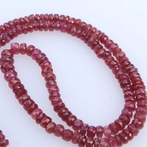 May include: A strand of faceted, deep red gemstone beads. The beads are strung together, forming a necklace or bracelet. The gemstones have a polished, reflective surface, and are arranged in a circular pattern.