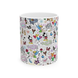 May include: White ceramic mug with a colorful doodle design featuring Mickey Mouse, Minnie Mouse, Tinkerbell, and other Disney characters. The mug has the text "Walt Disney World" and "Disneyland" on it.