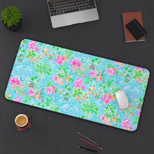 May include: A rectangular mousepad with a vibrant, tropical floral pattern in shades of pink, green, and orange on a light blue background. The design includes cartoon characters and castle illustrations. A white mouse rests on the pad.