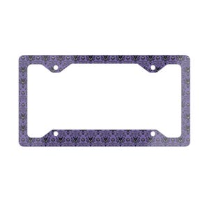 Puede incluir: Marco de matrícula morado con un patrón repetido de siluetas de casas encantadas negras. El marco tiene cuatro orificios de montaje y forma rectangular.