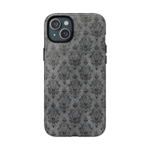 May include: A smartphone case with a gray, textured background featuring a repeating black gothic damask pattern. The case has a camera cutout and black side buttons. The design is reminiscent of vintage wallpaper.