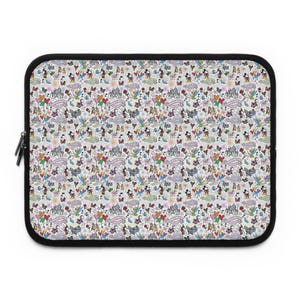 以下が含まれることがあります： 黒いジッパーとトリムが付いた長方形のラップトップスリーブ。スリーブは、白い背景にさまざまな色の漫画のキャラクター、城、ハート、風船の繰り返しパターンが特徴です。