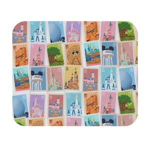 May include: A rectangular mat with rounded corners, covered in a collage of colourful postage stamps. The stamps showcase castles, landmarks, and a Mickey Mouse Ferris wheel, in shades of pink, blue, yellow, and green. Some stamps display the word "STUDIO".