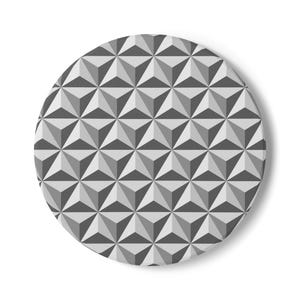 May include: A circular object featuring a repeating geometric pattern of triangles in shades of gray, white, and black. The design creates a three-dimensional effect with alternating light and dark triangular facets arranged in a symmetrical grid.