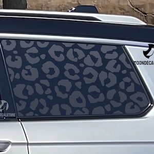 May include: A black car with a leopard print window decal. The decal is on the back passenger window and features a gray and black leopard print pattern. The decal has the text "MOONDECALSTORE" on the bottom right corner.