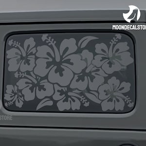 May include: A gray car with a gray hibiscus flower decal on the back window. The decal is a silhouette of a cluster of hibiscus flowers.