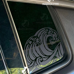 May include: A gray wave design car decal with a stylized wave pattern. The decal is placed on the back window of a car. The decal has the text "MOONDECALSTORE" on it.