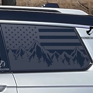 May include: A black and white car window decal featuring a mountain range silhouette with a US flag design. The decal has the text "MOONDECALSTORE" in the top right corner.