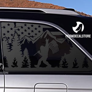 May include: A black and white silhouette decal of a person hiking in the mountains with an American flag. The decal is applied to the back window of a silver SUV. The decal includes the text "MOONDECALSTORE".