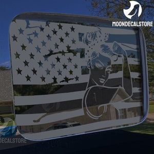 K&ouml;nnte beinhalten: Ein wei&szlig;er Vinyl-Aufkleber einer Frau mit erhobenem Arm in einer Faust, &uuml;berlagert mit einem verwitterten Design der amerikanischen Flagge. Der Aufkleber befindet sich auf einem schwarzen Hintergrund.