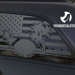 May include: A black car with a rear window decal featuring a white silhouette of a palm tree, sunset, and American flag. The decal also includes the text "MOONDECALSTORE".