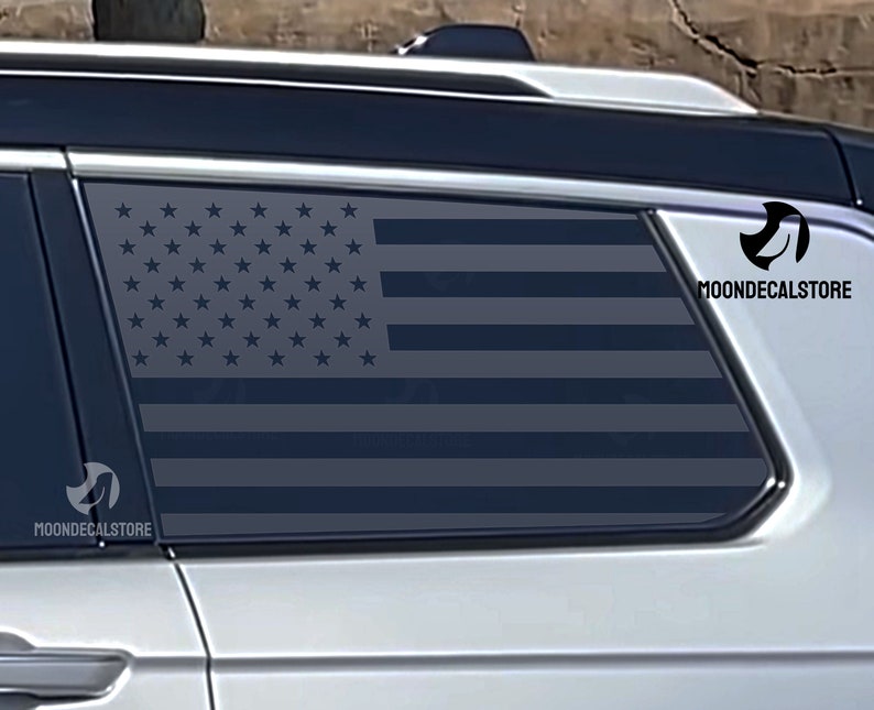 May include: A black and white American flag decal applied to the rear window of a silver SUV. The decal is visible through the tinted window. The decal is from the company "Moondecalstore".
