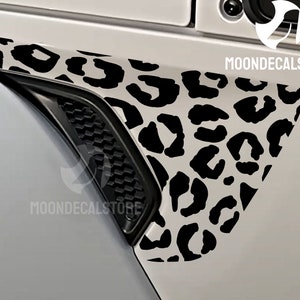 May include: Black and white leopard print decal for a car. The decal is on the side of a white car, near the wheel well.