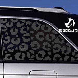 May include: A black car with a leopard print decal on the back window. The decal is a dark gray color and covers the entire window. The decal has the text "MOONDECALSTORE" on the top right corner.