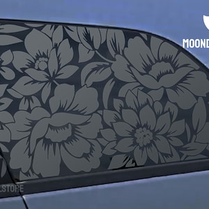 May include: A car window with a floral decal. The decal is a dark gray color and features a large floral pattern. The decal is on the back window of the car. The text "MOONDECALSTORE" is visible on the car.