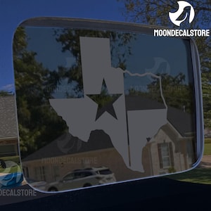 May include: A gray decal of the state of Texas with a star in the center, applied to a vehicle window. The decal is a silhouette of the state's outline. The text "MOONDECALSTORE" is visible in the upper right corner and lower left corner.